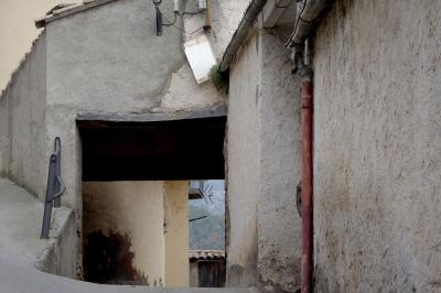 photograph “XI.2021 — Faces of home, 152” par David Farreny — www.farreny.net — Espagne, España, Espanya, Spain, Catalogne, Cataluña, Catalunya, Lérida, Lleida, Alt Urgell, Coll de Nargó, bourgade, town, village, maison, house, murs, walls, passage, rue, street, ciment, cement, barrière, guardrail, métal, metal, balcon, balcony, antenne, antenna, tuiles, tiles, gouttière, drainpipe, gutter, entrée, entrance