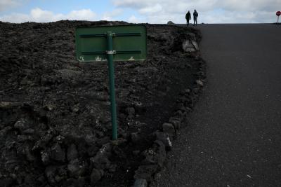 photograph “II.2018 — Lancerotte, 38” par David Farreny — www.farreny.net — winter, hiver, clouds, nuages, asphalt, asphalte, blacktop, bitume, stone, pierre, metal, métal, stop, woman, femme, man, homme, couple, travellers, voyageurs, tourists, touristes, people, gens, roadsigns, signs, routiers, panneaux, road, route, lava, lave, island, île, Lancerotte, Lanzarote, Canarias, Canary, Canaries, Spain, España, Espagne