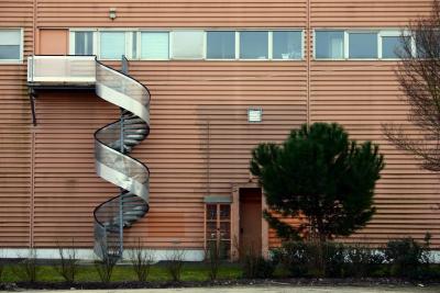 photograph “II.2005” par David Farreny — www.farreny.net — France, Aquitaine, Gironde, Floirac, hypermarché, hypermarket, mur, wall, paroi, métal, metal, tôle ondulée, corrugated iron, escalier, hélicoïdal, spirale, colimaçon, spiral, staircase, helical, marches, steps, pin, pine tree, arbres, trees, haie, hedge, fenêtres, windows, portes, doors, herbe, grass