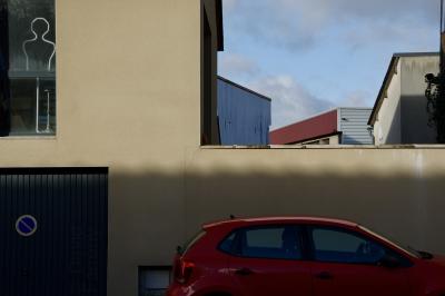 photograph “I.2015 — Fatigue at the window” par David Farreny — www.farreny.net — France, bâtiments, buildings, béton, concrete, garage, panneau, sign, fenêtre, window, voiture, car, rouge, red, ombre, shadow, mannequin, model, dummy, silhouette, outline, forme, shape, humaine, human, nuages, clouds, mur, wall, tôle ondulée, corrugated iron, métal, metal, Occitanie, Aveyron, Rouergue, Rieupeyroux