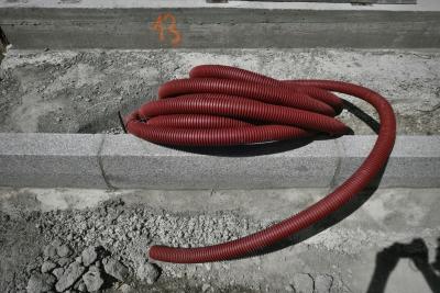 photograph “VIII.2023 — 13” par David Farreny — www.farreny.net — Andorre, Andorra, Canillo, route, road, travaux, chantier, works, béton, concrete, trottoir, pavement, sol, soil, earth, pierre, stone, tuyau, pipe, serpent, snake, plastique, plastic, rouge, red, nombre, number, peinture, paint, orange, 13, pierres, cailloux, stones, pebbles, ombre, shadow, photographe, photographer, gris, grey, gray