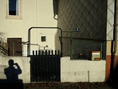 photograph “XII.2013 — Approaches to Christmas, 9” par David Farreny — www.farreny.net — France, maison, house, portail, gate, bois, wood, ciment, cement, plaque, numéro, number, plate, 3, boîte aux lettres, letterbox, mailbox, gouttière, drainpipe, métal, metal, grillage, clôture, fence, fencing, cour, yard, courtyard, fenêtres, windows, murs, walls, ombre, shadow, autoportrait, self-portrait, étendoir, clothes line, climatisation, air conditioning, unité extérieure, external unit, Mitsubishi, verre, vitre, glass, rideau, curtain, rue, street, feuilles, mortes, dead, leaves, Noël, Christmas, profusion, Occitanie, Aveyron, Rouergue, Olemps