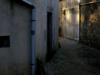 photograph “II.2015” par David Farreny — www.farreny.net — France, Occitanie, Aveyron, Rouergue, Balsac, ruelle, alley, lane, village, ciment, cement, gouttière, drainpipe, porte, door, portail, gate, garage, gravier, gravel, soir, evening, hiver, winter, métal, metal, pierre, stone, soleil, sun, lumière, light, vitre, verre, glass