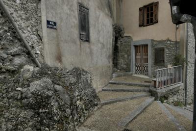 photograph “VI.2021 — Faces of home, 121” par David Farreny — www.farreny.net — France, Occitanie, Ariège, Tarascon-sur-Ariège, rue du Château de Lamothe, rocher, rock, maisons, houses, murs, walls, fenêtres, windows, porte, door, volets, shutters, bois, wood, pierre, stone, gouttières, drainpipes, plaque, plate, escalier, marches, steps, stairs, staircase, rambarde, guardrail, grille, railings, ruban, adhésif, tape, fil, wire, câble, cable, banc, bench, vide, empty, emptiness, désert, desert, domicile, home