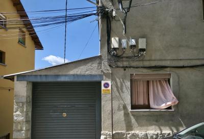 photograph “VII.2023 — Faces of home, 277” par David Farreny — www.farreny.net — Espagne, España, Spain, Catalogne, Cataluña, Catalunya, Catalonia, Gérone, Girona, Baixa Cerdanya, Basse-Cerdagne, Cerdagne, Cerdanya, Puigcerdà, ville, city, rue, street, maisons, houses, ciment, cement, béton, concrete, pierre, stone, câbles, cables, fils, wires, fenêtres, windows, stores, panneau, sign, stationnement interdit, no parking, rideau, curtain, vent, wind, rose, pink, verre, vitre, glass, voiture, car, boîtiers, boxes, toit, roof, garage, portail, gate, domicile, home