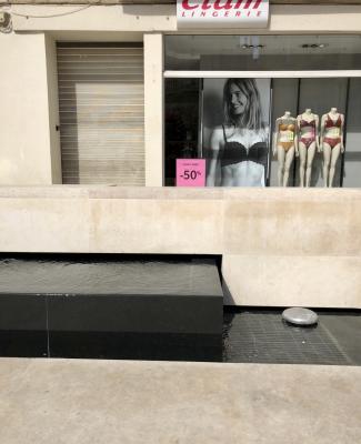 photograph “IX.2018 — Dream -50%” par David Farreny — www.farreny.net — France, Occitanie, Gascogne, Gascony, Gers, Auch, magasin, boutique, shop, store, Etam, lingerie, mannequins, vitrine, window, baie, bay, vitre, glass, verre, femme, woman, soutiens-gorge, bras, culottes, panties, plastique, plastic, photographie, photograph, photo, modèle, model, blonde, jeune, young, enseigne, sign, porte, door, blind, métal, metal, câble, cable, fil, wire, fontaine, fountain, publicité, advertising, pub, ad, affiche, poster, -50 %, soldes, sale, eau, water, pierre, stone, grille, grid, lovely week, étiquettes, tags, prix, price