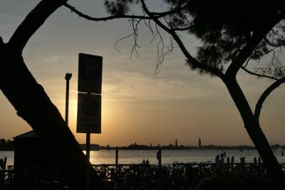 photograph “V.2022 — Signs” par David Farreny — www.farreny.net — Italie, Italia, Italy, Vénétie, Veneto, Venise, Venice, Venezia, Venexia, Lido, port, harbour, harbor, mer, sea, lagune, lagoon, Adriatique, Adriatic, eau, water, panneaux, signs, soir, evening, arbres, trees, pins, pines, soleil, sun, coucher, sunset, rambarde, guardrail, troncs, trunks, promeneurs, passers-by, vélos, bikes, bicyclettes, bicycles, ciel, sky, carte postale, postcard