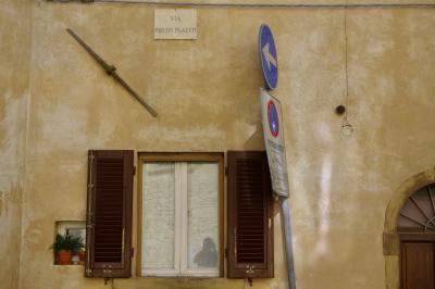photograph “X.2019” par David Farreny — www.farreny.net — Italie, Italia, Italy, Toscane, Toscana, Tuscany, Pise, Pisa, Volterra, rue, street, maison, house, mur, wall, façade, facade, fenêtre, window, porte, door, bois, wood, volets, shutters, pots, panneau, sign, routier, roadsign, flèche, arrow, gauche, left, métal, metal, reflet, vitre, verre, glass, photographe, photographer, plaque, plate, pierre, stone, via Persio Flacco, câble, cable, fil, wire, beige