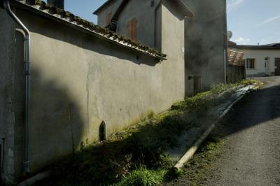 photograph “II.2025 — Whatever” par David Farreny — www.farreny.net — France, Occitanie, Gascogne, Gascony, Lomagne, Gers, Saint-Clar, village, rue, street, montée, côte, climb, bitume, blacktop, asphalte, asphalt, mur, wall, ciment, cement, gouttière, drainpipe, maison, house, métal, metal, toit, roof, tuiles, tiles, fenêtres, windows, door, porte, herbe, grass, pierre, stone, bois, wood, mousse, moss, parabole, satellite, dish, cheminée, chimney, meuble, furniture, ombre, shadow