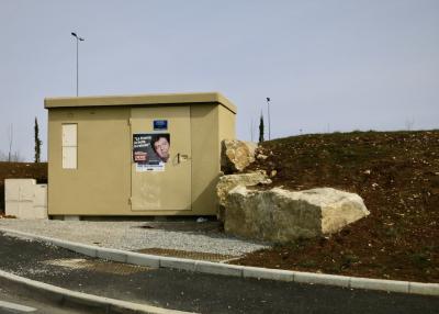 photograph “III.2012 — Political rot” par David Farreny — www.farreny.net — France, Occitanie, Aveyron, Rouergue, Sébazac-Concourès, route, road, bitume, blacktop, asphalte, asphalt, poste, électrique, electricity, post, transformateur, transformer, porte, door, affiche, poster, election, Jean-Luc Mélenchon, clown, démagogue, populiste, populist, demagogue, crapule, scoundrel, millionnaire, millionaire, parasite, autocrate, autocrat, La France la belle la rebelle, slogan, ridicule, ridiculous, Front de Gauche, échec, failure, rocher, rock, terre, earth, sol, soil, trottoir, pavement, gravier, gravel, lampadaires, lamps, métal, metal, talus, bank, arbres, trees, cyprès, cypresses, collaborateurs, collaborators