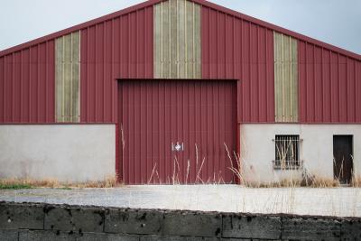 photograph “VII.2011 — Annual closure” par David Farreny — www.farreny.net — France, industrie, industry, entrepôt, warehouse, tôle ondulée, corrugated iron, rouge, red, jaune, yellow, façade, facade, muret, low wall, parpaings, breeze-blocks, portail, gate, fenêtre, window, porte, door, herbes, grasses, graminées, grille, bars, Occitanie, Aveyron, Rouergue, Manhac