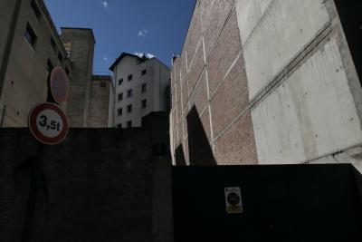 photograph “VI.2021” par David Farreny — www.farreny.net — Andorre, Andorra, Andorre-la-Vieille, Andorra la Vella, capitale, capital, ville, city, immeubles, bâtiments, buildings, brique, brick, béton, concrete, toit, roof, palissade, palisade, mur, wall, murs, walls, panneaux, routiers, signs, roadsigns, ombre, shadow, pénombre, darkness, sombre, dark, angles, coins, corners, fenêtres, windows, cour, yard, courtyard, gouttière, drainpipe, ciel, sky, laid, ugly, laideur, ugliness