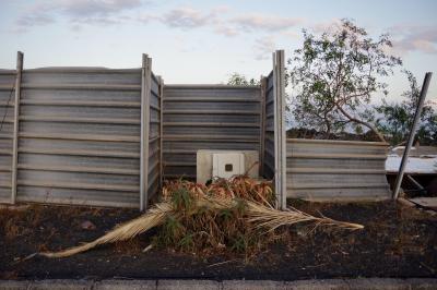 photograph “V.2016 — Lancerotte, 40” par David Farreny — www.farreny.net — Espagne, España, Spain, Canaries, Canarias, Canary, Lanzarote, Lancerotte, île, island, tôle ondulée, corrugated iron, palissade, fence, stockade, chantier, building site, arbre, tree, autel, altar, palmes, palm leaves, soir, evening, métal, metal, trottoir, pavement, nuages, clouds, Teguise, Costa Teguise