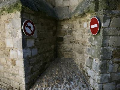 photograph “VI.2015 — Double bind” par David Farreny — www.farreny.net — France, Occitanie, Tarn, Sorèze, mur, wall, pierre, stone, renfoncement, niche, recoin, recess, panneaux, signs, routiers, roadsigns, sens interdit, one way, interdiction de tourner, gauche, banned turn, left, face-à-face, face to face, opposition