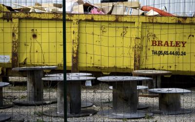 photograph “IV.2008 — Braley” par David Farreny — www.farreny.net — France, Occitanie, Aveyron, Rouergue, Olemps, benne, dumpster, métal, metal, Braley, numéro, téléphone, telephone, number, phone, cartons, boxes, cardboard, planches, planks, bois, wood, tuyau, pipe, plastique, plastic, rouge, red, jaune, yellow, mur, paroi, wall, gravier, gravel, bobines, tourets, reels, grillage, fence, clôture, fencing, rouille, rust, rusty