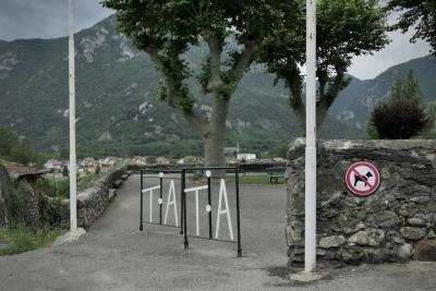 photograph “VI.2021” par David Farreny — www.farreny.net — France, Occitanie, Ariège, Tarascon-sur-Ariège, Pyrénées, Pyrenees, montagnes, mountains, ville, city, bourgade, town, jardin, garden, mur, wall, pierre, stone, poteaux, posts, poles, métal, metal, panneau, sign, chien, dog, interdit, forbidden, arbres, trees, platanes, plane trees, bancs, benches, maisons, houses, barrières, guardrails, initiales, initials, TA, TATA, lettres, letters, T, A, caractères, characters, muret, low wall, esplanade, belvédère, terrasse, terrace, bitume, blacktop, asphalte, asphalt, forêt, forest, bois, wood