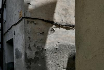 photograph “V.2023 — Whatever” par David Farreny — www.farreny.net — Espagne, Spain, España, Catalogne, Cataluña, Catalunya, Lleida, Lérida, Alt Urgell, La Seu d'Urgell, ville, city, rue, street, ciment, cement, maison, house, porte, door, vieux, old, ombre, shadow, pénombre, darkness, sombre, dark, câbles, cables, fils, wires, ruelle, alley, coin, corner, angle, rugueux, rough, plaque, plate, carrer Les Eres, gris, gray, grey