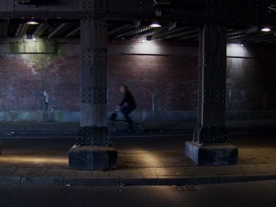 photograph “X.2017” par David Farreny — www.farreny.net — Pays-Bas, Netherlands, Nederland, Hollande, Holland, Amsterdam, passage, souterrain, underground, gare, station, Amsterdam Centraal, piliers, pillars, métal, metal, rue, street, rivets, brique, brick, lumières, lights, lampes, lamps, cycliste, cyclist, vélo, bike, trottoir, pavement, bitume, blacktop, asphalte, asphalt, béton, concrete, ville, city, flou, blur