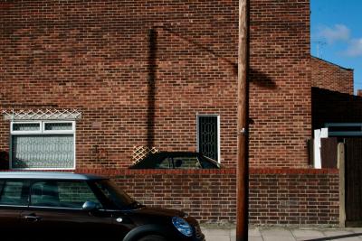 photograph “X.2010 — Faces of home, 21” par David Farreny — www.farreny.net — Royaume-Uni, United Kingdom, Angleterre, England, GB, UK, Londres, London, Greenwich, maisons, houses, brique, brick, antenne, aerial, antenna, bois, wood, ville, city, fenêtres, windows, voitures, cars, noires, black, métal, metal, poteau, post, lampadaire, réverbère, lamp, street lamp, rue, street, ombre, shadow, domicile, home, mur, wall, muret, low wall, trottoir, pavement, métropole, metropolis, portail, porte, gate, treillis, trellis, grille, bars