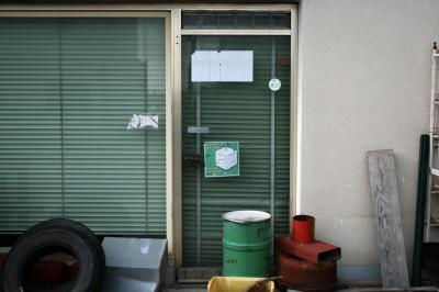 photograph “XII.2009 — Mineral lick” par David Farreny — www.farreny.net — France, Occitanie, Aveyron, Rouergue, La Primaube, magasin, shop, atelier, workshop, vitrine, window, verre, vitre, glass, store, porte, door, métal, metal, mur, wall, pneu, tire, tyre, bidon, can, planche, plank, bois, wood, poignée, handle, affiche, poster, autocollant, sticker, pierre à lécher, bloc à lécher, pierre à sel, mineral lick, salt lick, toute l'année, all year long, matériel, material