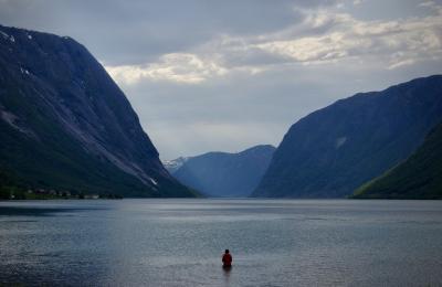 photograph “VI.2019 — Run away to the North, 199” par David Farreny — www.farreny.net — Norvège, Norge, Norway, Vestland, Sunnfjord, Skei i Jølster, Skei, Kjøsnesfjorden, fjord, eau, water, montagnes, mountains, man, homme, young, jeune, pêcheur, fisherman, fisher, ciel, sky, nuages, clouds, maisons, houses, neige, snow, carte postale, postcard, Lunde, Sogn og Fjordane