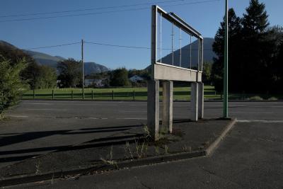 photograph “IX.2018” par David Farreny — www.farreny.net — France, Nouvelle-Aquitaine, Aquitaine, Pyrénées-Atlantiques, Arudy, route, road, montagne, mountain, panneau, affichage, display, billboard, vide, empty, emptiness, trottoir, pavement, bitume, blacktop, asphalte, asphalt, poteaux, électriques, electricity, posts, poles, arbres, trees, ciment, cement, pré, meadow, maisons, houses, câbles, cables, fils, wires, Pyrénées, Pyrenees