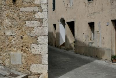 photograph “VIII.2022 — Faces of home, 154” par David Farreny — www.farreny.net — Italie, Italia, Italy, Toscane, Toscana, Tuscany, Sienne, Siena, San Quirico d'Orcia, rue, street, coin, corner, angle, pierre, stone, mur, wall, portes, doors, fenêtres, windows, ombre, shadow, grille, railings, plantes, plants, volets, shutters, bois, wood, domicile, home