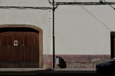 photograph “X.2021” par David Farreny — www.farreny.net — Espagne, España, Spain, Catalogne, Cataluña, Catalunya, Catalonia, Lérida, Lleida, Sort, rue, street, maison, house, mur, wall, paroi, garage, portail, gate, porte, door, voiture, car, poubelle, bin, trash, pierre, stone, brique, brick, gouttière, drainpipe, métal, metal, câbles, cables, fils, wires, ombre, shadow, bois, wood, trottoir, pavement, panneau, sign