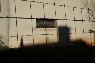 photograph “II.2015 — Whatever” par David Farreny — www.farreny.net — France, Occitanie, Aveyron, Rouergue, Olemps, hiver, winter, maison, house, fenêtre, window, soir, evening, grille, railings, clôture, fence, fencing, lumière, light, ombre, shadow, béton, concrete, métal, metal, mur, wall, crépi, roughcast, branches, branchages, arbre, tree, cheminée, chimney, coin, corner, angle, neige, snow, dépression, depression