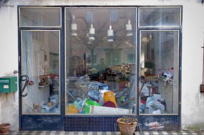 photograph “II.2014 — Self-portrait with obsolescence” par David Farreny — www.farreny.net — France, magasin, shop, fermé, closed down, vitrine, window, verre, vitre, glass, bordel, mess, monstrueux, horrendous, désordre, untidiness, objets, objects, portes, doors, lampes, lamps, boîte à lettres, letterbox, mailbox, pots de fleurs, plant pots, flowerpots, autoportrait, selfportrait, reflet, reflection, poignées, handles, carrelage, tiling, arbres, trees, profusion, Occitanie, Aveyron, Rouergue, Réquista