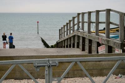 photograph “V.2013 — Curb your speed” par David Farreny — www.farreny.net — Royaume-Uni, United Kingdom, Grande-Bretagne, Great Britain, Angleterre, England, UK, GB, Sussex, West Sussex, Arun, Bognor Regis, front de mer, seafront, mer, sea, Manche, Channel, horizon, épi, groyne, brise-lames, breakwater, bois, wood, barrière, gate, métal, metal, cadenas, lock, rampe, ramp, slope, cale, mise à l'eau, launch, launching, slipway, béton, concrete, panneaux, signs, curb your speed, attention, no parking, jeune fille, girl, jeune homme, garçon, boy, blonde, déchets, détritus, litter, rubbish