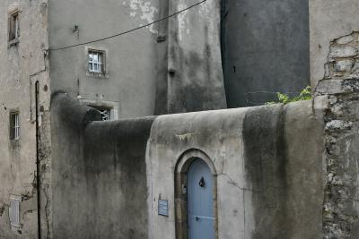 photograph “VII.2020 — Faces of home, 114” par David Farreny — www.farreny.net — France, Auvergne, Rhône-Alpes, Haute-Loire, Le Monastier-sur-Gazeille, ville, city, rue, street, maison, house, gris, grey, gray, mur, wall, pierre, stone, ciment, cement, porte, door, câble, cable, fil, wire, fenêtres, windows, grilles, railings, angle, coin, corner, vieux, old, domicile, home