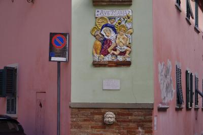 photograph “X.2019” par David Farreny — www.farreny.net — Italie, Italia, Italy, Toscane, Toscana, Tuscany, Pise, Pisa, San Miniato, Saint-Miniatus, ville, city, rue, street, brique, brick, bas-relief, low relief, Ave Maria, religion, catholicisme, catholicism, catholique, catholic, christianisme, christianism, Vierge, Marie, Virgin, Mary, Jésus, Jesus, Christ, panneau, routier, sign, roadsign, mur, wall, fenêtres, windows, volets, shutters, bois, wood, voiture, car, métal, metal, rose, pink, porte, door, stationnement interdit, no parking
