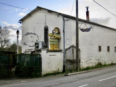 photograph “XII.2024 — Whatever” par David Farreny — www.farreny.net — France, Occitanie, Gascogne, Gascony, Lomagne, Tarn-et-Garonne, Beaumont-de-Lomagne, entrepôt, warehouse, brocanteur, second-hand dealer, brocante, flea market, portails, gates, métal, metal, poteaux, posts, poles, ciment, cement, mur, wall, maison, house, toit, roof, cheminée, chimney, arbre, tree, enseigne, sign, bateau, boat, personnage, figure, lion, route, road, bitume, blacktop, asphalte, asphalt, trottoir, pavement, gouttière, drainpipe, gutter, câbles, cables, fils, wires, branches, branchages, statue, sculpture, art, lampadaire, lamp
