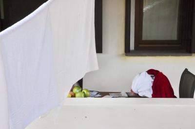 photograph “V.2014 — Schoolgirl at the work table” par David Farreny — www.farreny.net — Italie, Italy, Italia, Sardaigne, Sardinia, Sardegna, Sardigna, Nuoro, Orosei, collégienne, schoolgirl, jeune fille, girl, serviette, towel, turban, chaise, chair, table, muret, low wall, fil à linge, washing line, clothes line, pommes, apples, vert, green, rouge, red, travail, work, écriture, rédaction, writing, penchée, bent over, béton, concrete, blanc, white, fenêtre, window, verre, glass, Lu*