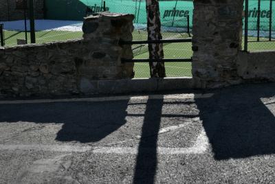photograph “I.2022” par David Farreny — www.farreny.net — Andorre, Andorra, Canillo, rue, street, bitume, blacktop, asphalte, asphalt, muret, low wall, pierre, stone, arbre, tree, tronc, trunk, ombre, shadow, tennis, court, filet, net, vert, green, bâche, sheet, publicité, advertising, pub, ad, Prince, neige, snow, rambarde, guardrail, métal, metal, grillage, fencing