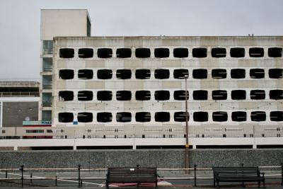 photograph “V.2013 — Multistorey” par David Farreny — www.farreny.net — Royaume-Uni, United Kingdom, Grande-Bretagne, Great Britain, Angleterre, England, UK, GB, Sussex, West Sussex, Worthing, front de mer, seafront, parking, car park, bâtiment, building, étages, multi-storey, parking garage, parkade, ouvertures, openings, néon, neons, neon, lights, tour, tower, béton, concrete, verre, glass, métal, metal, projecteurs, floodlights, barrière, guardrail, bancs, benches, rue, street, lampadaire, réverbère, lamp, bowling, enseigne, sign, profusion