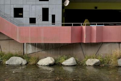 photograph “XI.2022 — CS” par David Farreny — www.farreny.net — Andorre, Andorra, Canillo, rivière, river, eau, water, Valira d'Orient, rochers, rocks, édifice, bâtiment, building, parking, car park, béton, concrete, rambarde, guardrail, métal, metal, rampe, railing, ouvertures, openings, rectangles, tag, CS, miroir, mirror, arbuste, shrub, rose, pink