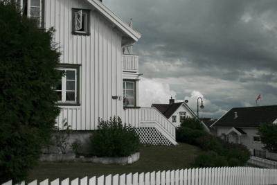 photograph “VII.2012 — Run away to the North, 21. Approaching cloud at Åsgårdstrand” par David Farreny — www.farreny.net — Norvège, Norway, Norge, Vestfold, Åsgårdstrand, maisons, houses, bois, wood, blanc, blanches, white, clôture, fence, fenêtres, windows, balcon, balcony, haie, hedge, herbe, grass, escalier, stairs, nuages, clouds, orage, tempête, storm, drapeaux, flags, norvégiens, Norwegian, lampadaire, street lamp, 2