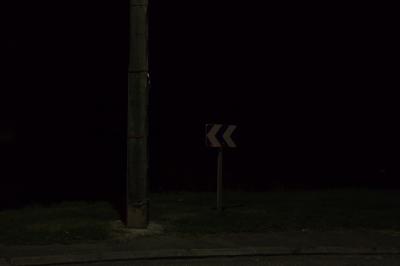 photograph “VIII.2015 — At night” par David Farreny — www.farreny.net — France, Occitanie, Gascogne, Gascony, Gers, Jegun, nuit, night, rue, street, poteau, post, pole, ciment, cement, panneau, sign, routier, roadsign, virage, bend, trottoir, pavement, métal, metal, noir, blank, pénombre, darkness, sombre, dark