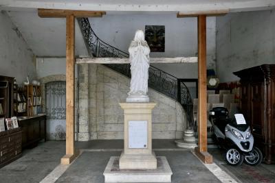 photograph “V.2025 — Supported spirituality (II)” par David Farreny — www.farreny.net — France, Occitanie, Gascogne, Gascony, Lomagne, Gers, Lectoure, antiquités, brocante, antiques, flea market, Village des Brocanteurs, Second-hand dealers' Village, vieux, objets, old, objects, métal, metal, pierre, stone, bois, wood, porte, door, time, temps, passé, past, statue, Vierge, Virgin, femme, woman, fiction, religion, catholicisme, Catholicism, christianisme, Christianism, socle, base, étais, props, three-wheeled, scooter, trois roues, à vendre, for sale, affiche, poster, annonce, announce, meubles, furniture, livres, books, escalier, staircase, rampe, railing, chaises, chair, tableau, peinture, painting, visage, face, yeux, eyes, regard, look, tiroirs, drawers, plaque, plate, prière, prayer
