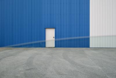 photograph “VI.2012” par David Farreny — www.farreny.net — France, zone industrielle, industrial, park, estate, industrie, industry, tôle ondulée, corrugated iron, bitume, blacktop, asphalte, asphalt, métal, metal, porte, door, verre, vitre, glass, fenêtre, window, voiture, car, bleu, blue, blanc, white, gris, grey, gray, Occitanie, Aveyron, Rouergue, Rodez, Onet-le-Château