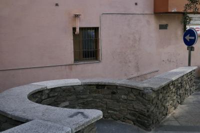 photograph “VI.2021” par David Farreny — www.farreny.net — Andorre, Andorra, ville, city, rue, street, muret, low wall, pierre, stone, mur, wall, béton, concrete, fenêtre, window, grille, railings, cheminée, chimney, câble, cable, métal, metal, panneau, routier, sign, roadsign, flèche, arrow, gauche, left, branche, branch, feuilles, leaves, rampe, banister, enseignes, magasins, shops, signs, Pompes Fúnebres Andorranes, Escaldes-Engordany