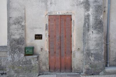 photograph “II.2014 — 12” par David Farreny — www.farreny.net — France, Occitanie, Aveyron, Rouergue, Réquista, rue, street, maison, house, ciment, cement, gris, grey, gray, porte, door, volets, shutters, gouttière, drainpipe, carrelage, tiling, boîte à lettres, letterbox, mailbox, plage, plate, nom, name, Solange Cayre, orthophoniste, speech therapist, sur rendez-vous, on appointment, pierre, stone, numéro, number, 12