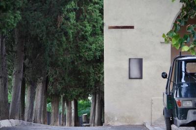 photograph “VIII.2022” par David Farreny — www.farreny.net — Italie, Italia, Italy, Toscane, Toscana, Tuscany, Sienne, Siena, San Quirico d'Orcia, rue, street, mur, wall, coin, corner, angle, arbres, trees, troncs, trunks, cèdres, cedars, feuillage, foliage, trottoir, pavement, poubelle, trash, bin, feuilles, leaves, véhicule, vehicle, triporteur, three-wheeled, Ape 50, Piaggio, phare, headlight, rétroviseur, mirror, bitume, blacktop, asphalte, asphalt