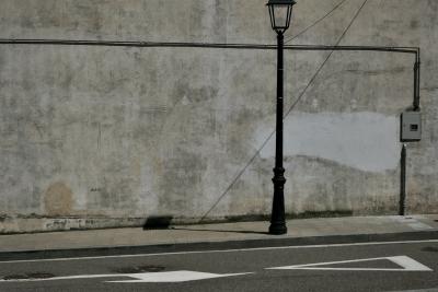 photograph “VI.2020” par David Farreny — www.farreny.net — Espagne, Spain, España, Catalogne, Catalonia, Cataluña, Catalonha, Lleida, Aran, Vielha, Vielha e Mijaran, Viella, ville, city, rue, street, mur, wall, ciment, cement, gris, grey, gray, câble, cable, fil, wire, tuyau, pipe, gouttière, drainpipe, lampadaire, lamp, ombre, shadow, trottoir, pavement, flèche, arrow, triangle, asphalte, asphalt, bitume, blacktop, armoire, box, métal, metal