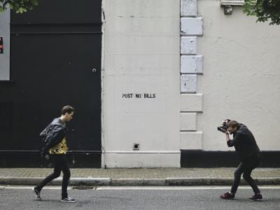 photograph “VIII.2015 — Obsolete young star” par David Farreny — www.farreny.net — Royaume-Uni, United Kingdom, Grande-Bretagne, Great Britain, Angleterre, England, Londres, London, City, Cité, rue, street, mur, wall, inscription, sign, Post no bills, Affichage interdit, trottoir, pavement, feuillage, foliage, bitume, blacktop, asphalte, asphalt, hommes, men, photographe, photographer, appareil photo, camera, modèle, model, jeune, young, vanité, vanity