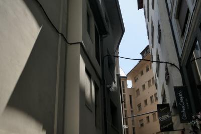photograph “VI.2021” par David Farreny — www.farreny.net — Andorre, Andorra, Andorre-la-Vieille, Andorra la Vella, ville, city, capitale, capital, rue, street, ruelle, alley, bâtiments, immeubles, buildings, béton, concrete, étroit, narrow, ombres, shadows, fenêtres, windows, magasins, shops, stores, angle, coin, corner, câbles, cables, fils, wires, toit, roof, joaillerie, jewelry, fleurs, flowers, panneaux, signs