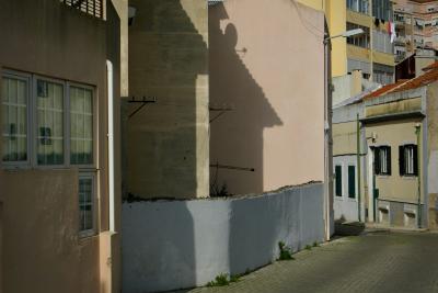 photograph “II.2020” par David Farreny — www.farreny.net — Portugal, Lisbonne, Lisboa, Lisbon, rue, street, maisons, houses, immeubles, bâtiments, buildings, béton, concrete, ciment, cement, mur, wall, muret, low wall, fenêtres, windows, toits, roofs, ombres, shadows, lampadaire, lamp, gouttière, drainpipe, fils, wires, câbles, cables, coin, corner, angle, linge, clothing, profusion, capitale, capital, ville, city