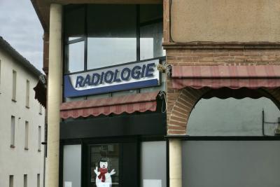 photograph “XII.2023 — Christmas gift” par David Farreny — www.farreny.net — France, Occitanie, Tarn-et-Garonne, Caussade, ville, city, bourgade, town, immeuble, building, bâtiment, cabinet, radiologie, radiology, office, enseigne, sign, angle, coin, corner, brique, brick, arche, arch, arc, vitrine, window, verre, vitre, glass, pilier, pillar, colonne, column, fenêtres, windows, illustration, bonhomme de neige, snowman, hiver, winter, stores, câbles, cables, fils, wires, crépi, roughcast, porte, door, ciel, sky, nuages, clouds